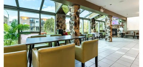 Glass-roofed room with stone columns, green chairs, tables and a fireplace
