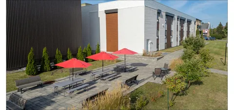 Brick residence wing beside a patio with red umbrellas and outdoor tables