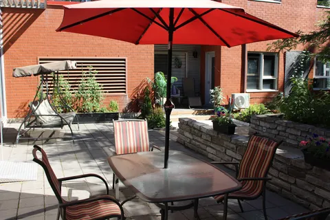 Patio with a red umbrella, striped chairs, a swing and raised planting beds