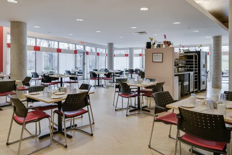 Dining room with tables set for meals, red-seated chairs and large windows