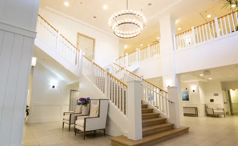 Lobby staircase beneath a chandelier, with seating and an upper-floor gallery.