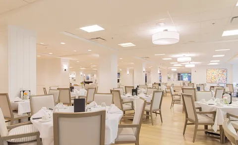 Dining room with tables, upholstered chairs and ceiling lights.