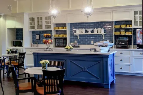 Cafe with a blue counter, tables, black chairs and shelves of cups and plates
