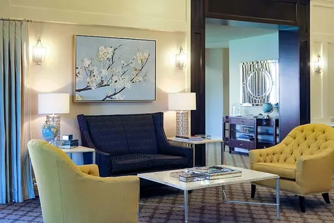 Sitting area with yellow armchairs, a blue sofa, a coffee table and floral artwork