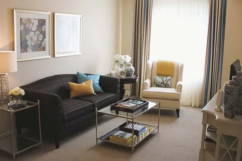 Sitting area with a dark sofa, cream armchair, glass coffee table and floral artwork