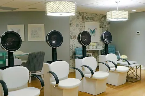 Salon with white chairs beneath hood dryers and butterfly artwork