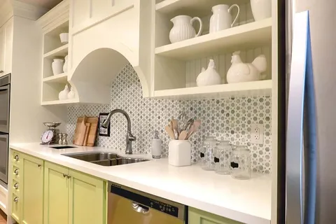 Kitchen counter with a sink, dishwasher, green cabinets and shelves of white dishes