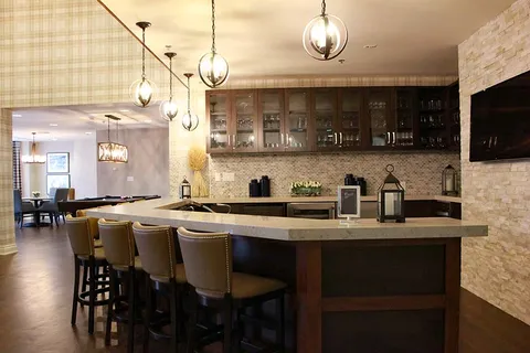 Bar with tall stools, pendant lights, cabinets and a television