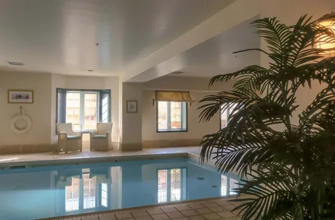 Indoor pool beside windows, wicker chairs and a large potted plant