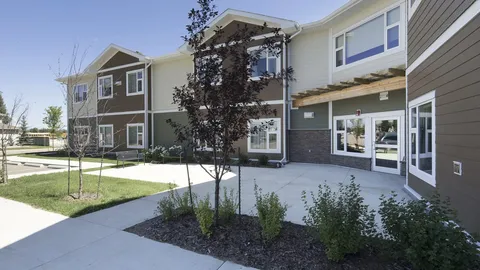 Two-storey residence exterior with windows, an entrance, lawn and young trees.