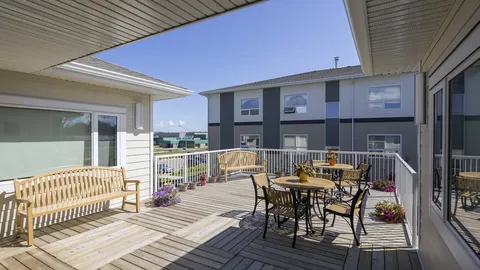 Covered deck with benches, tables, chairs, flower pots and a railing.