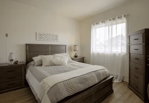 Bedroom with a wooden bed frame, dresser and curtained window