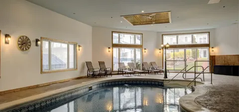 Indoor pool with handrails, lounge chairs and large windows