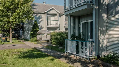 Low-rise residence with balconies, a garden swing and a paved path beside trees