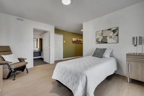 Bedroom with a single bed, reclining chair, cabinet and floral artwork