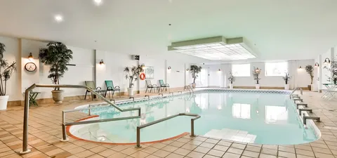 Indoor swimming pool with handrails, deck chairs and potted trees