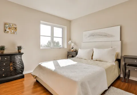 Bedroom with a cream bedspread, bedside tables and a tall chest of drawers