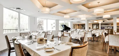 Dining room with set tables, upholstered chairs, pendant lights and a grand piano