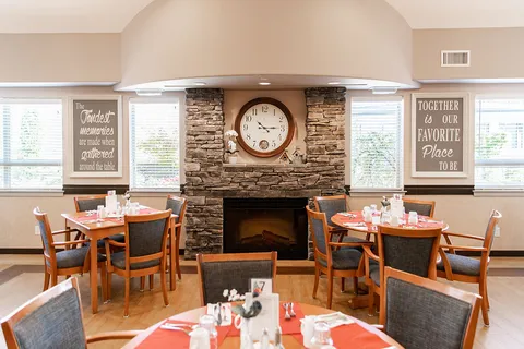 Dining room with wooden chairs, red place settings, a stone fireplace and a large clock