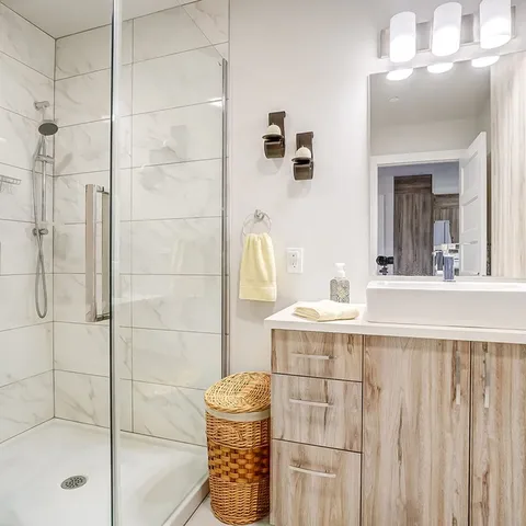 Bathroom with a glass shower enclosure, white sink, wood-grain vanity, mirror and wicker hamper