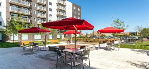 Patio tables beneath red umbrellas beside a lawn