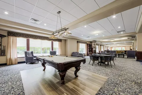 Room with a billiards table, game tables and seating beside large windows
