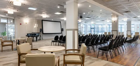 Room with rows of black chairs facing a blank projection screen
