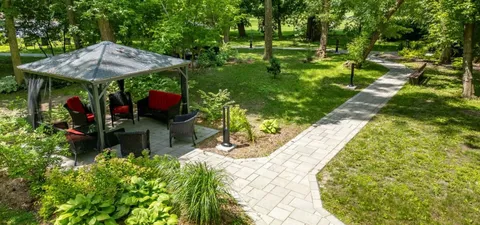 Garden path beside trees, lawns and a gazebo with outdoor chairs