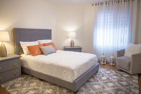 Bedroom with a grey upholstered bed, bedside tables, lamps, an armchair and a shag rug