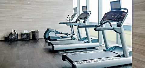 Treadmills and an elliptical machine beside tall windows