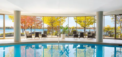 Indoor pool with floor-to-ceiling windows overlooking a river and autumn trees