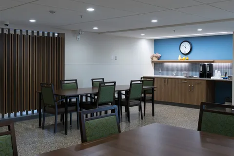 Dining tables with green chairs beside a countertop and cabinets