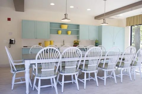 Room with a long table, white chairs, blue cabinets and yellow planters