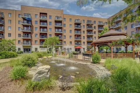 Brick residence with balconies behind a pond, fountain and wooden gazebo