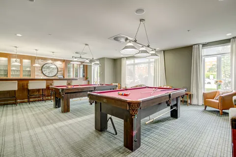 Room with two pool tables, a counter, tall stools and large windows
