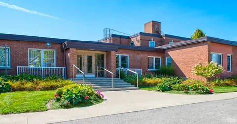 Brick building with an entrance ramp, steps and landscaped flowerbeds.