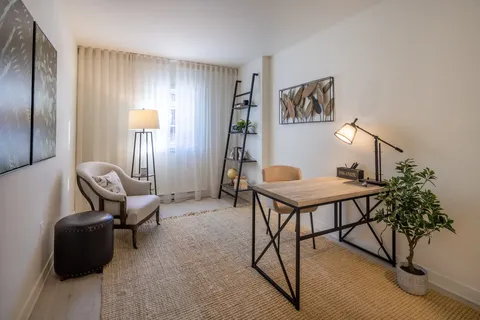 Room with a wooden desk, armchair, floor lamp and potted plants