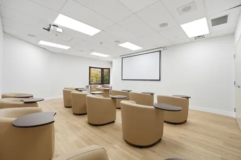 Screening room with upholstered chairs and a projection screen.