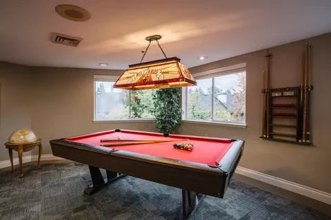 Pool table beneath a stained-glass light beside large windows