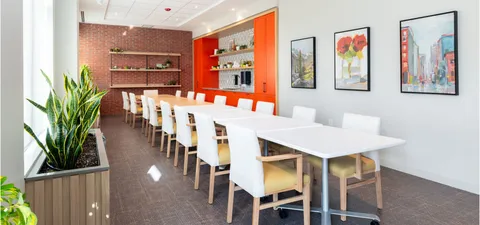 Long white tables and chairs beside a counter and three framed prints