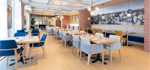 Dining tables and upholstered chairs beneath pendant lights beside a city mural