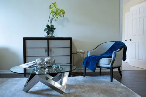 Room with a grey armchair, blue throw, glass coffee table, cabinet and yellow orchid