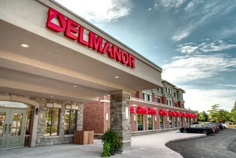 Covered entrance with stone pillars, glass doors and red awnings along the brick building