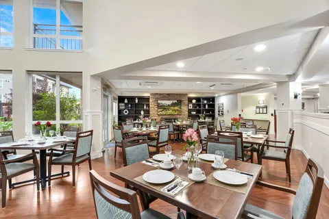 Dining tables beneath high windows beside shelving and a landscape painting