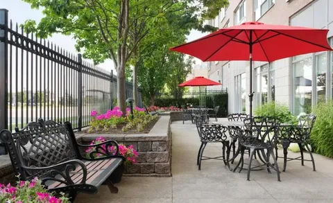 Patio tables, chairs and red umbrellas beside planted borders.