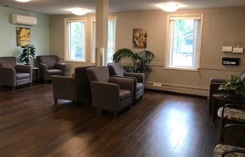 Room with upholstered armchairs, plants, framed pictures and large windows