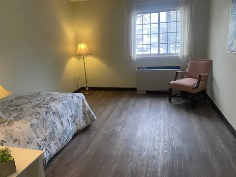 Room with a bed, upholstered chair, lamp and window