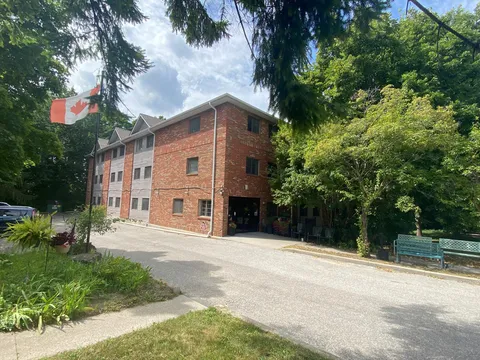 Brick building beside a paved driveway, trees and garden beds