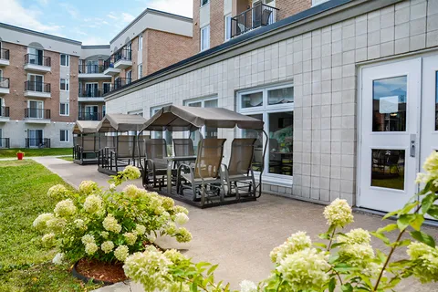 Covered patio swings beside flowering shrubs, lawn and the brick building