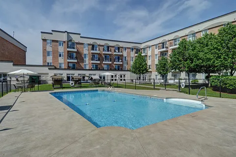 Outdoor swimming pool with handrails, a concrete deck and the brick building behind